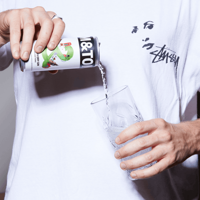 Man in a white tee pouring a can of Jim and Tonic London Dry Gin into a clear glass.