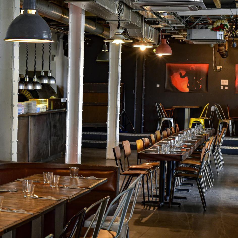 An inviting bar restaurant showcasing a long table adorned with clear glasses and plates. The industrial décor features metal accents, and the walls are decorated with vibrant artwork.